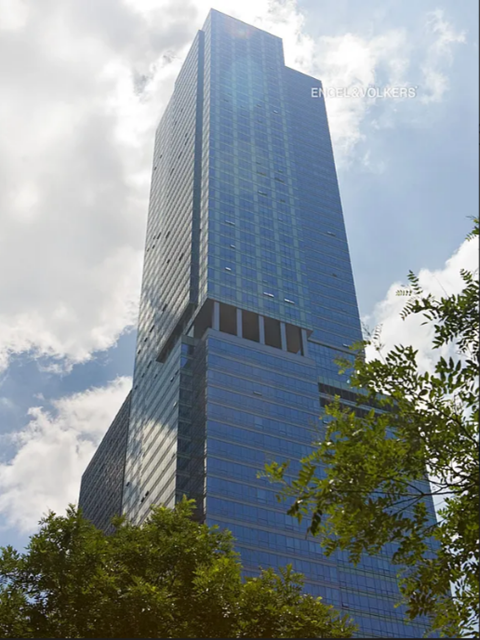 A tall skyscraper with a glass facade stands under a partly cloudy sky.