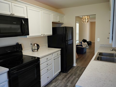A black refrigerator sits in a kitchen with white cabinets.