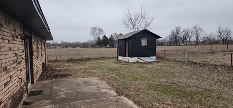 A small black shed sits in a grassy field.