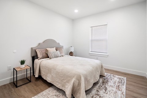 A bedroom with a bed, pillows, a small table, and a rug.