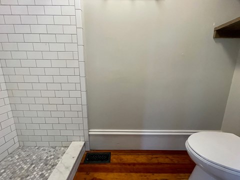 A white toilet sits next to a white tiled wall.