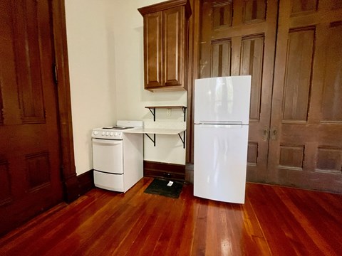A white refrigerator stands in a kitchen with wooden floors and cabinets.