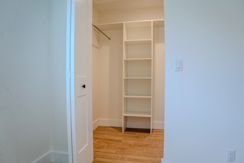 A white door opens to a room with a shelving unit and wooden floors.
