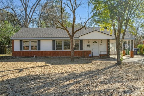 A small house with a white door and windows is surrounded by trees.