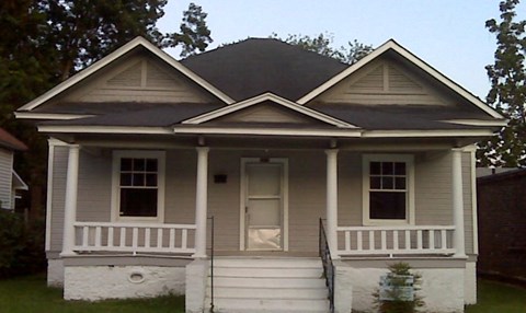 A small white house with a black roof and a porch.