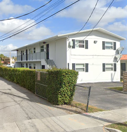 A white two-story house with a black fence and hedges on the side.