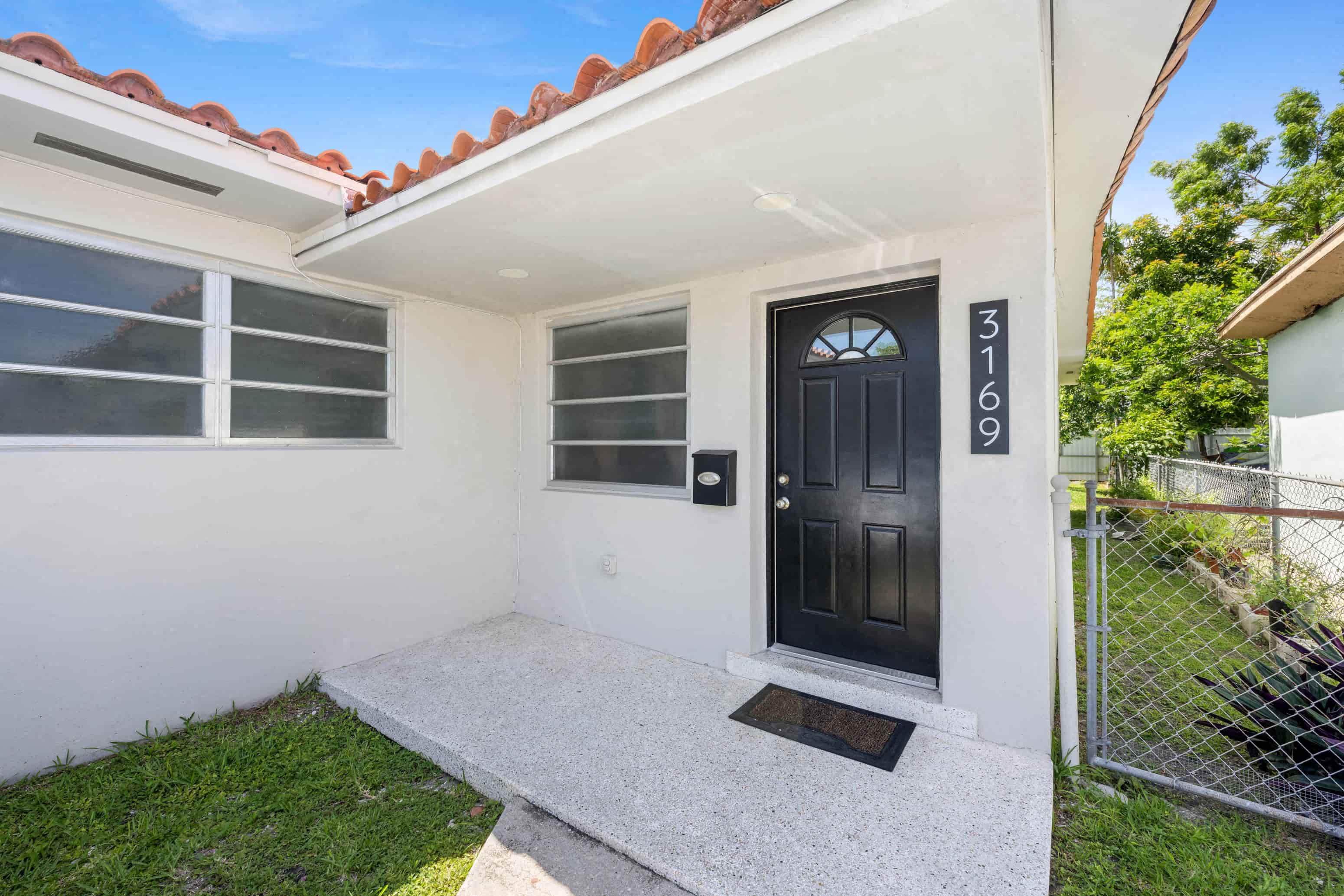 A white house with a black door and a mailbox on the wall.