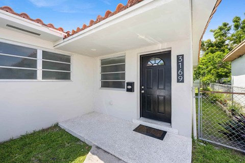 A white house with a black door and a mailbox on the wall.