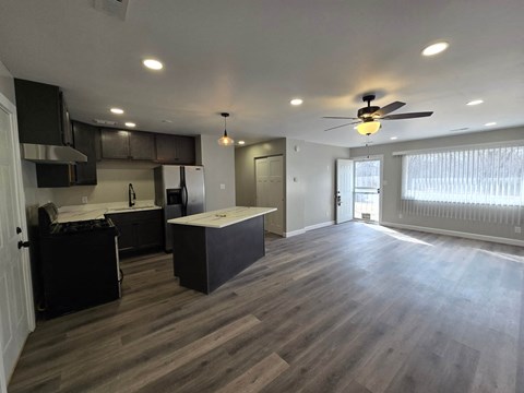 A spacious kitchen and living room with dark wood flooring and white walls.