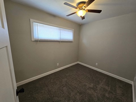 A room with a ceiling fan and a window with blinds.