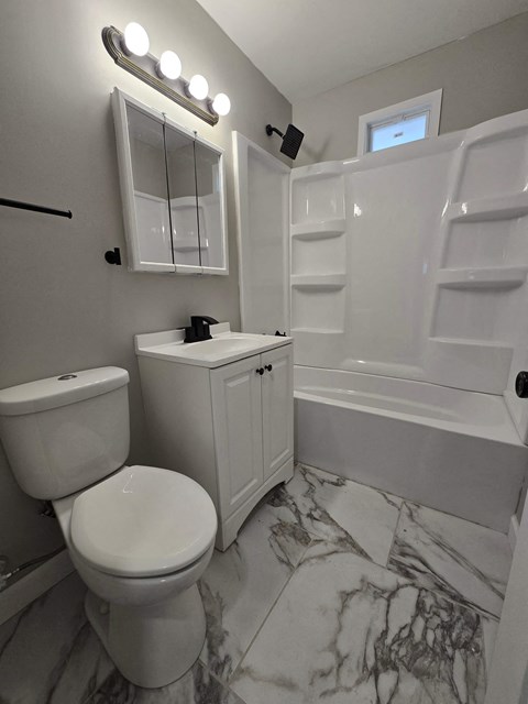A white toilet sits next to a white sink in a marble bathroom.