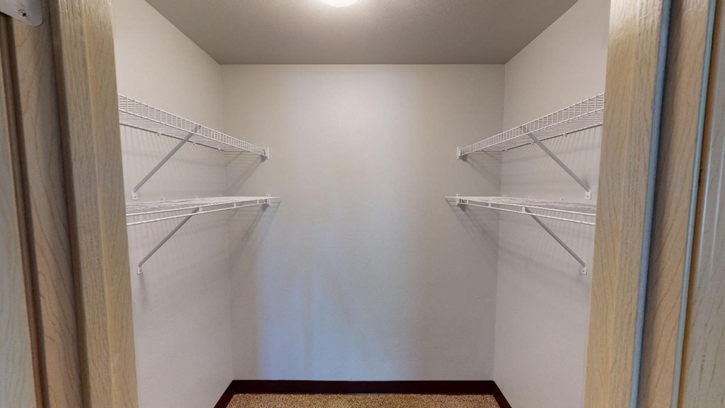 A walk-in closet with white shelves and a wooden floor.