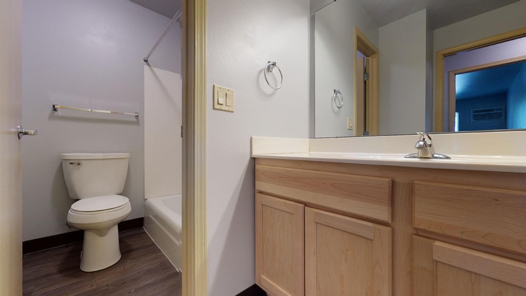 A white toilet is in a small bathroom with wood cabinets.