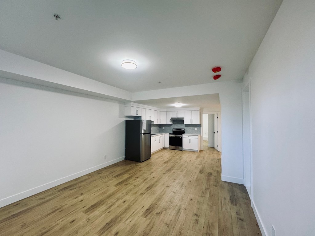 A kitchen area with a white wall and a wooden floor.