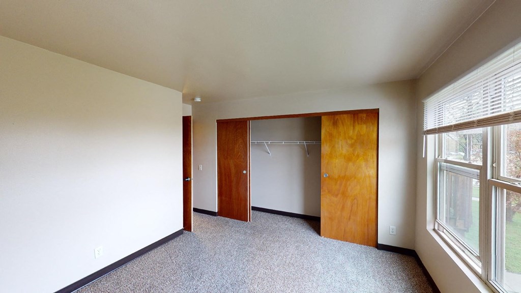 A room with a carpeted floor and a window with blinds.