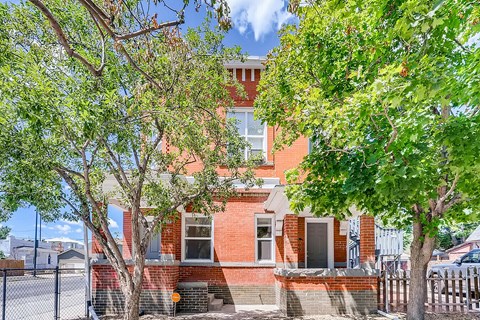 A red brick house with a black fence and trees in front.