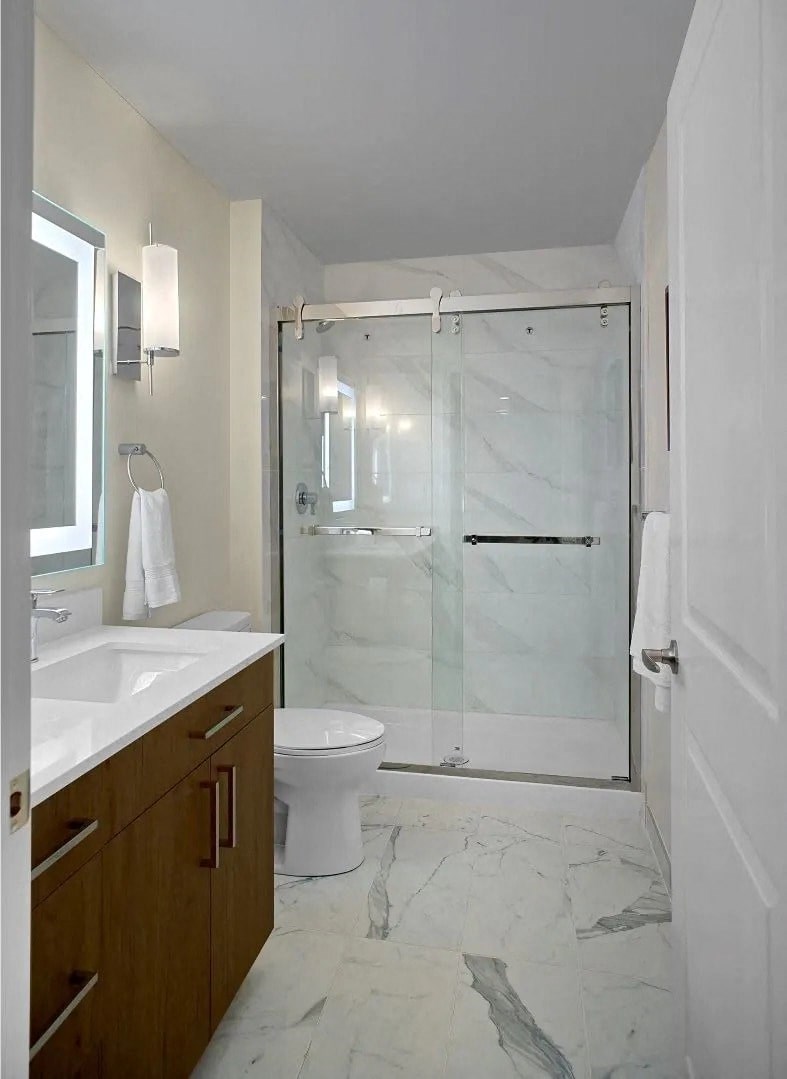 A white toilet sits in a bathroom with a walk-in shower.