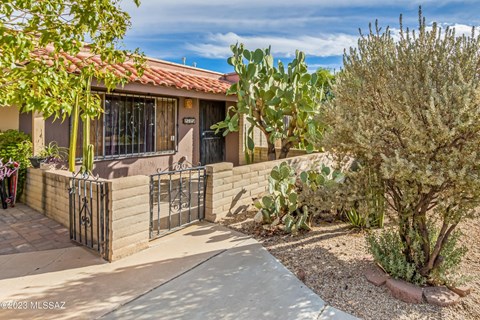 A house with a red tile roof and a gate surrounded by a garden.
