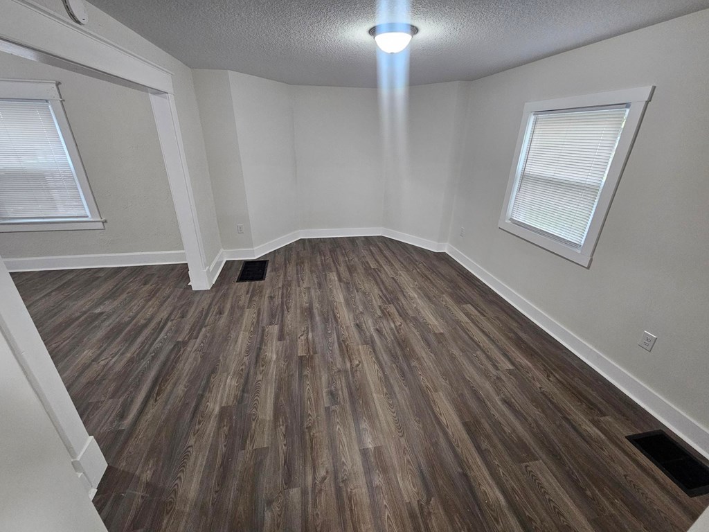 A room with wooden flooring and two windows.