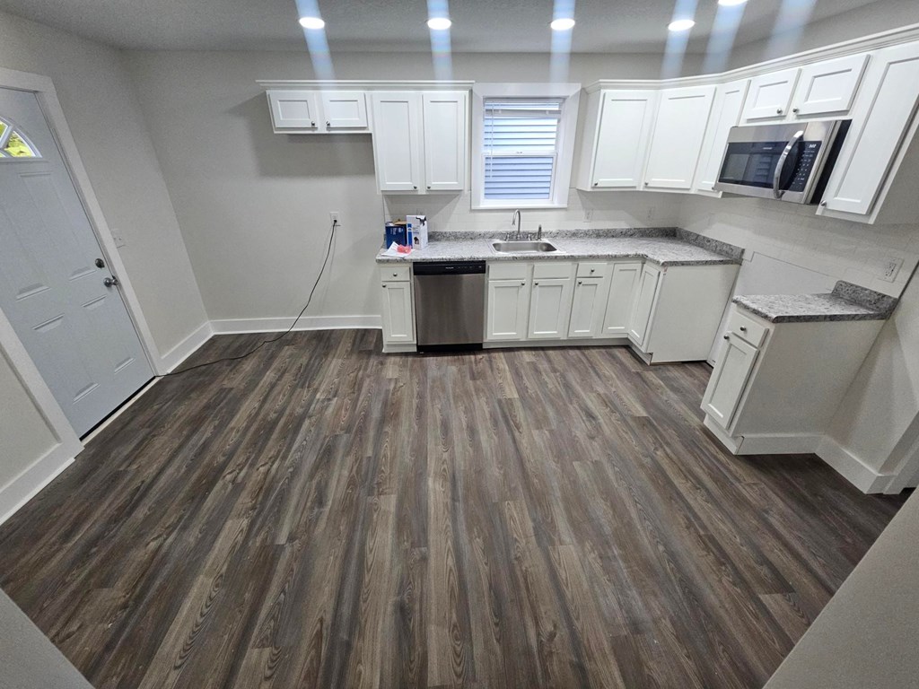 A kitchen with white cabinets and a wooden floor.