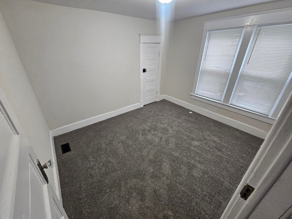A room with a carpeted floor, a window with blinds, and a door with a handle.