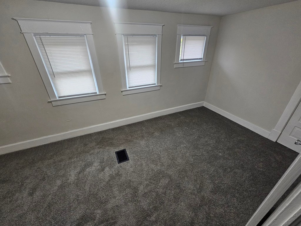 A room with grey carpet and three windows.
