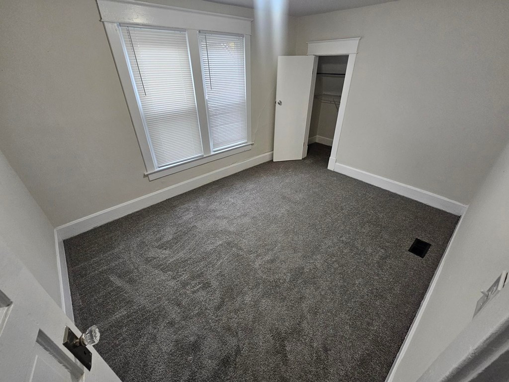 A room with a carpeted floor and a window with blinds.