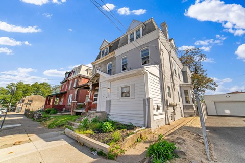 A white two-story house with a red brick house in the background.