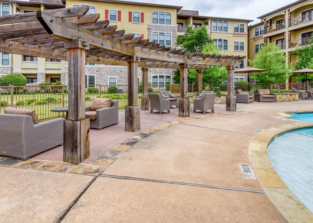 A pool area with a wooden pergola and lounge chairs.