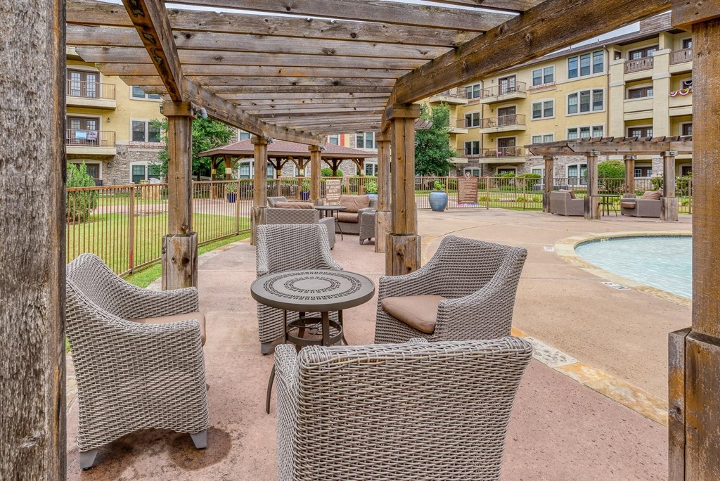 A patio with chairs and a table is covered by a wooden roof.