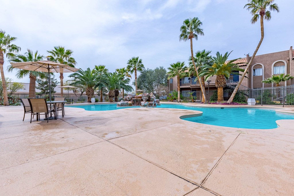 A pool surrounded by palm trees and a building in the background.