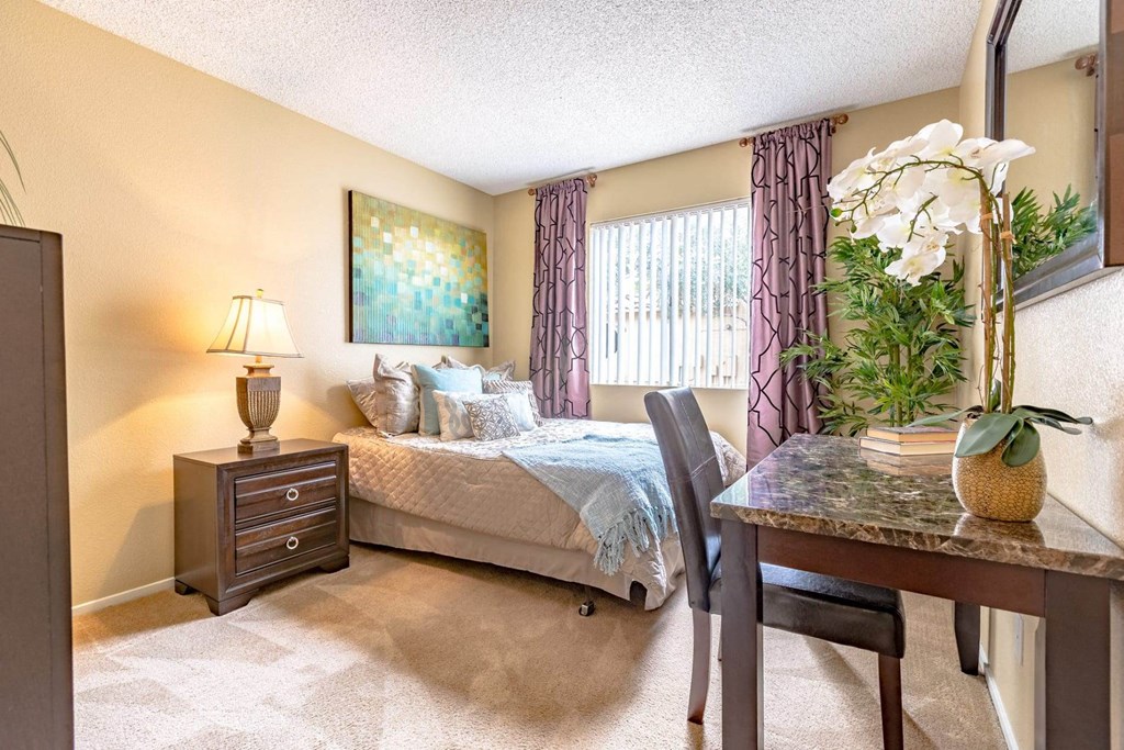 A bedroom with a bed, a chair, a nightstand, and a painting on the wall.