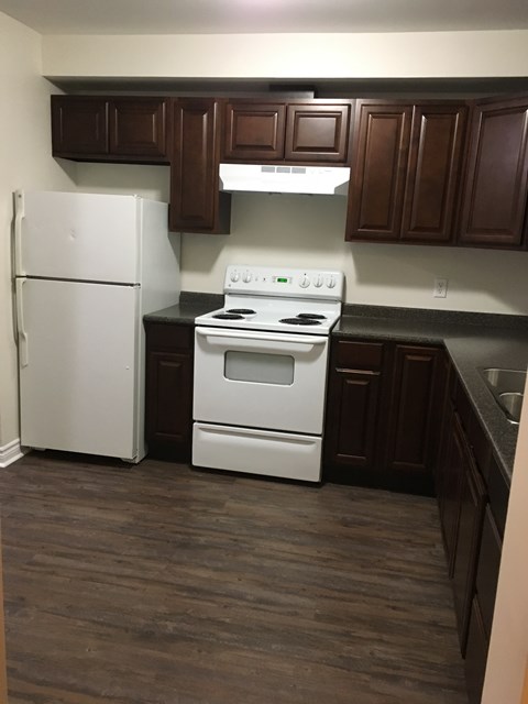 A white refrigerator stands next to a white stove in a kitchen with dark wood cabinets.