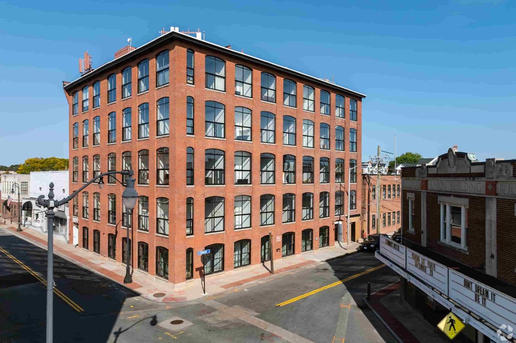 A red brick building with many windows is on a street corner.