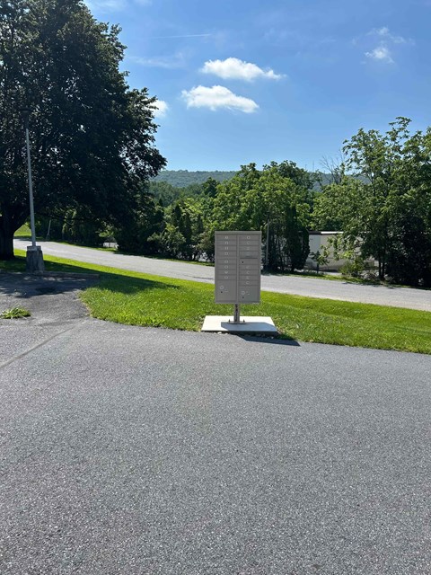 A signpost stands in the middle of a paved area with trees in the background.