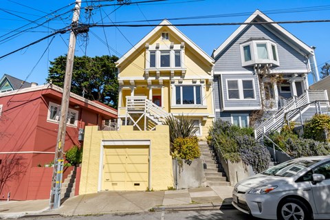 A white car is parked in front of a yellow house.