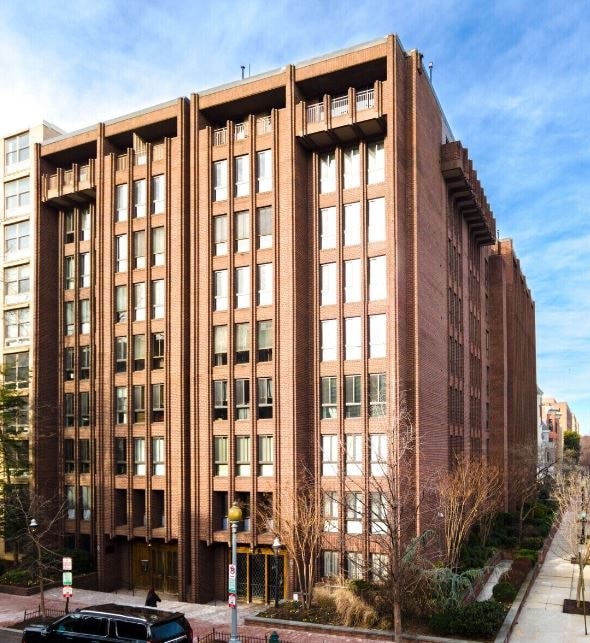 A large red brick building with many windows and a car parked in front.