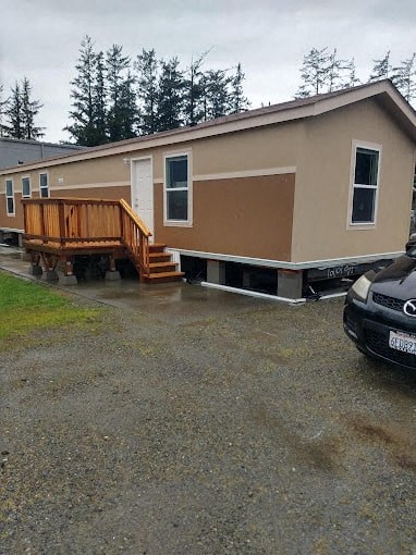 A beige mobile home with a wooden deck and a car parked in front.