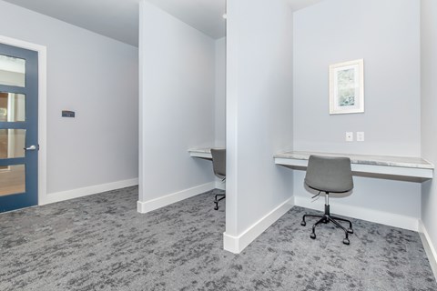 A room with a grey carpet and a white desk with a chair.