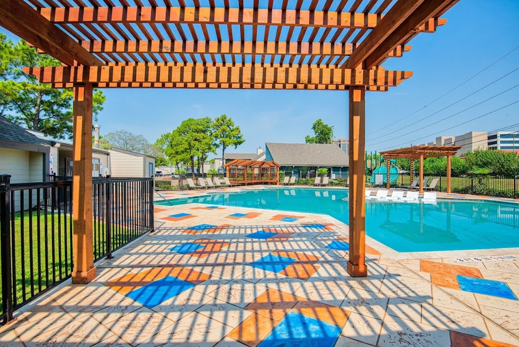 A pool area with a colorful tile walkway and a wooden pergola.