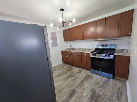 A kitchen with a black fridge, wooden cabinets, and a black stove top oven.