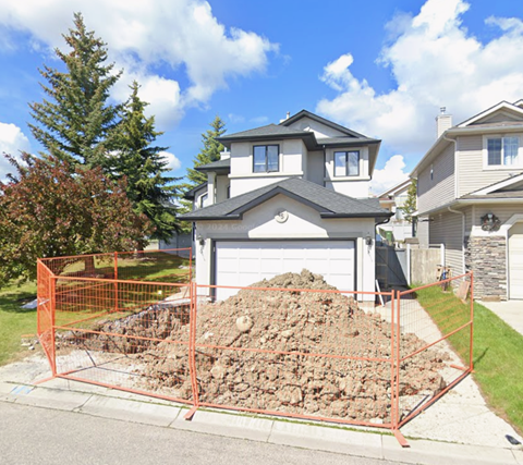 A pile of rocks is surrounded by an orange fence in front of a house.