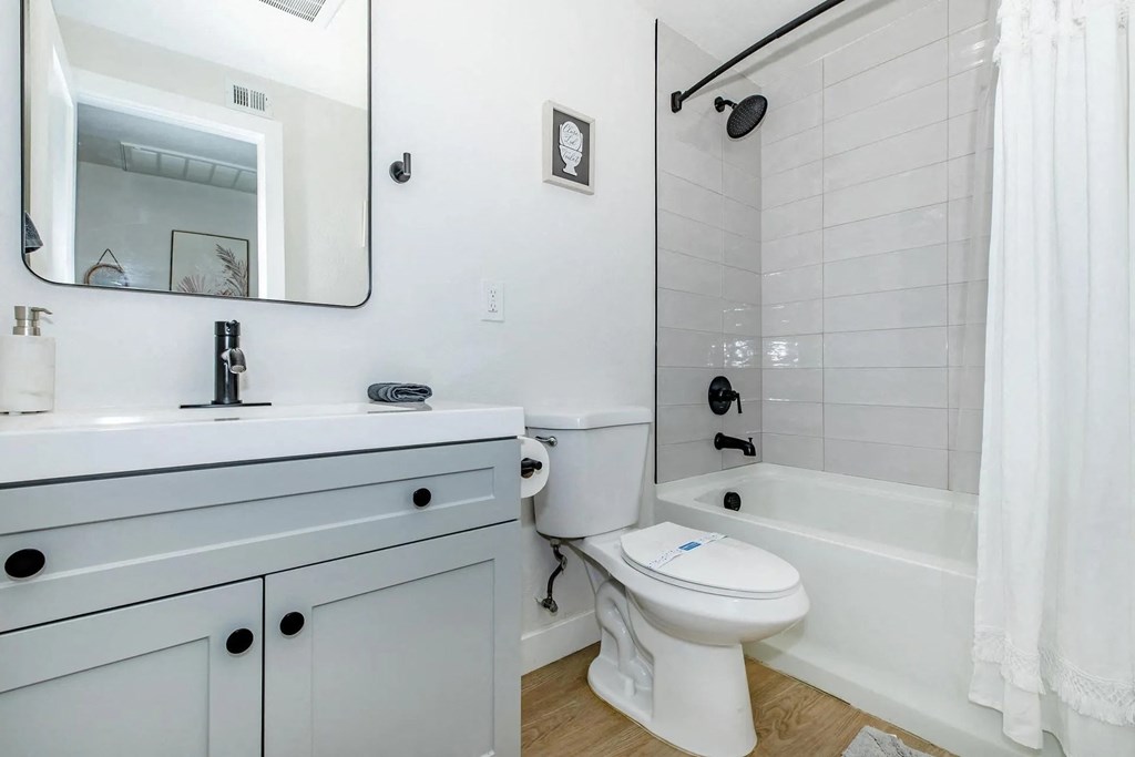 A white toilet with a blue sticker on the lid is in a bathroom with a white tub and a white shower curtain.