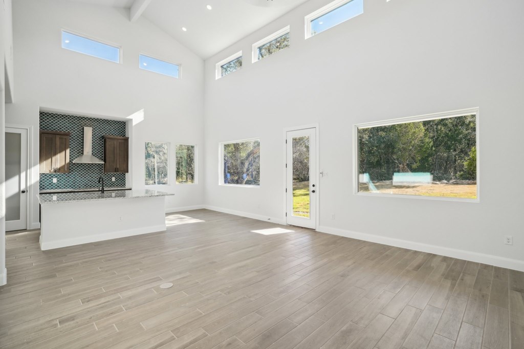 A spacious room with wooden floors and white walls, featuring a kitchen area with a stove and a countertop, as well as several windows and pictures on the walls.