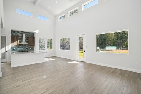 A spacious room with wooden floors and white walls, featuring a kitchen area with a stove and a countertop, as well as several windows and pictures on the walls.