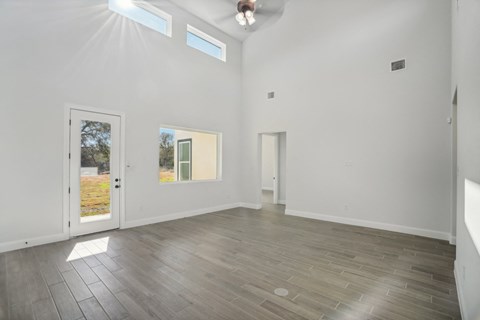 A room with white walls and a wooden floor with a door on the left and a window on the right.