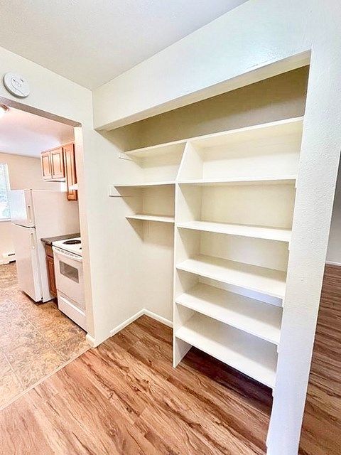 A white shelving unit in a kitchen with a refrigerator in the background.