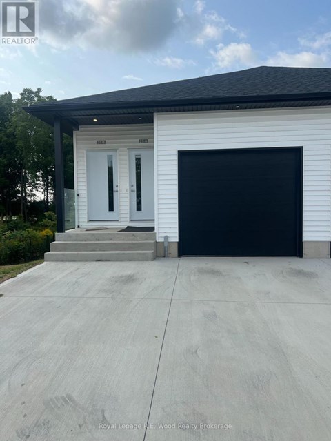 A white house with a black garage door and a realtor logo on the top left.