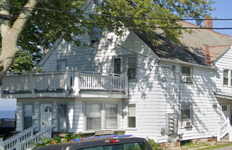 A white house with a balcony and a car parked in front.