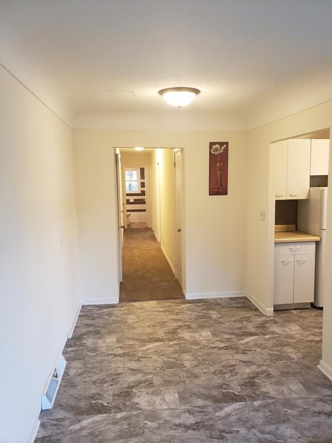 A hallway with a carpeted floor and a kitchen area at the end.